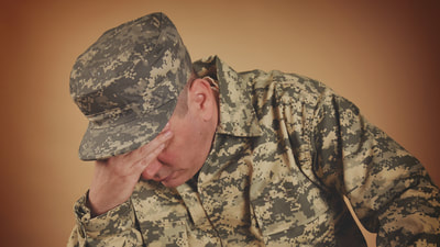 military man in fatigues who appears stressed or sad with head leaning on his hand